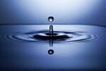 This photo shows a water droplet falling into a pool of water. The impact has created ripples on the surface of the water.