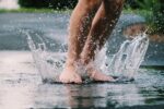 A person jumps barefoot into a puddle. Water splashes up around their feet.